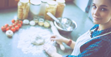 Güzel bir kadın mutfakta pasta pişiriyor. Masanın yanında duruyor.