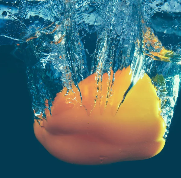 Färsk gul paprika plaska i vatten på svart bakgrund — Stockfoto