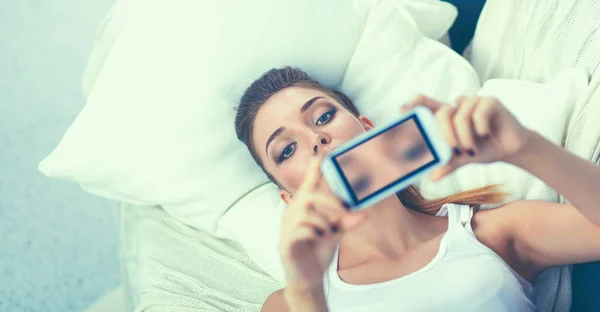 在卧室里，用她的手机就自己拍照的快乐布鲁内特 — 图库照片