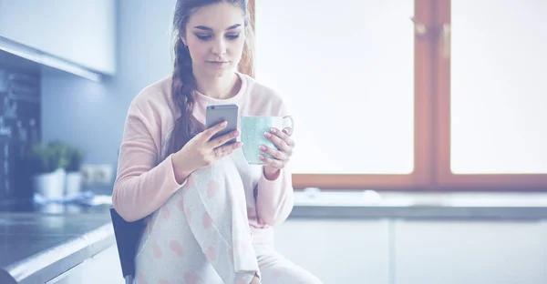 Mujer usando el teléfono móvil sentado en la cocina moderna — Foto de Stock