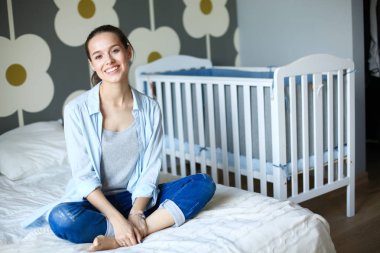 Yatakta çocuk karyolası yakın oturan bir genç bayan. Genç anne