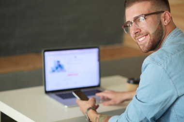 Genç adam kullanarak telefon ve dizüstü bilgisayarda çalışır.