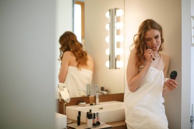 Telefon ile banyo üzerinde duran genç kadın.