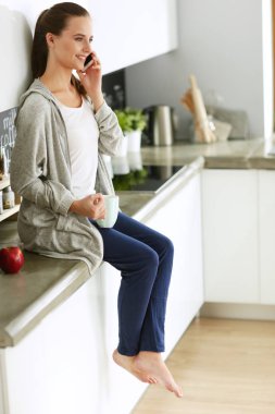 modern mutfakta otururken cep telefonu kullanan kadın.
