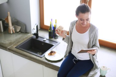 Mutfakta dijital tablet kullanan güzel genç bir kadın..