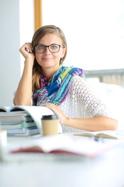 Kitapların arasında bir masada oturan genç bir kadın. Öğrenci