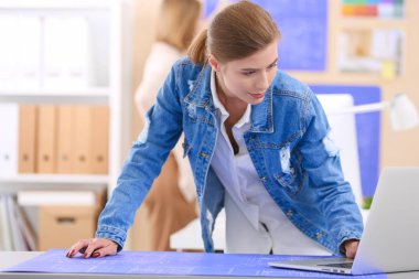 Masanın yanında duran iki genç kadın enstrüman, plan ve dizüstü bilgisayarla.