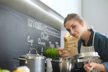 Mutfakta sobanın yanında duran genç bir kadın. .