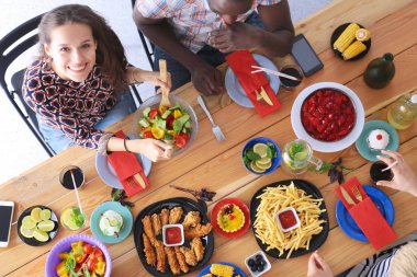 Ahşap masada otururken birlikte yemek yiyen bir grup insanın üst düzey görüntüsü. Masada yemek var. İnsanlar fast food yiyor..