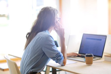 Ofis masasında oturan ve cep telefonuyla konuşan genç ve güzel bir iş kadını. İş kadını