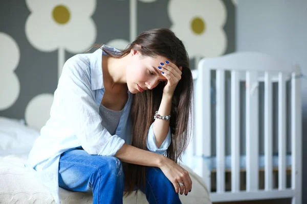 Ung trött kvinna som sitter på sängen nära barnens spjälsäng. Ung mamma. — Stockfoto