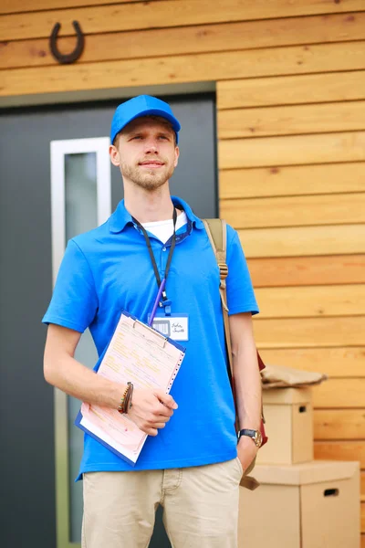 Mavi üniformalı gülümseyen kurye servis konseptine paket kutusu teslim eden teslimatçı. Mavi üniformalı gülümseyen teslimatçı.