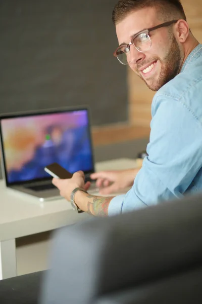 Jonge man met telefoon en werkt op de laptop. — Stockfoto