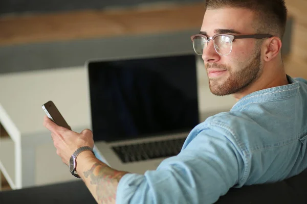 Jonge man met behulp van een telefoon en werken op een laptop. Student SMS op de telefoon. — Stockfoto