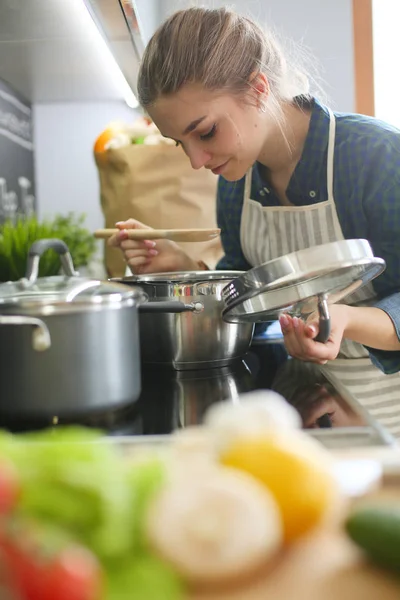 Tânără femeie în picioare de aragaz în bucătărie  . — Fotografie, imagine de stoc