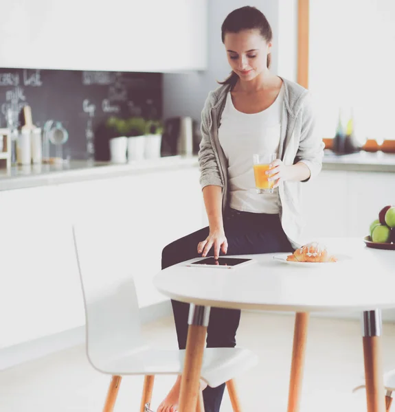 Mladá žena s pomerančovým džusem a tabletem v kuchyni. — Stock fotografie