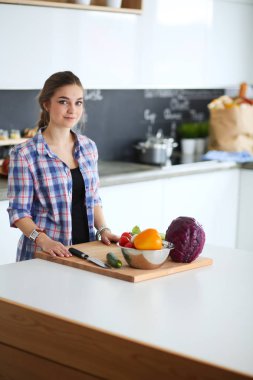 Masanın yanındaki mutfakta sebze doğrayan genç bir kadın..