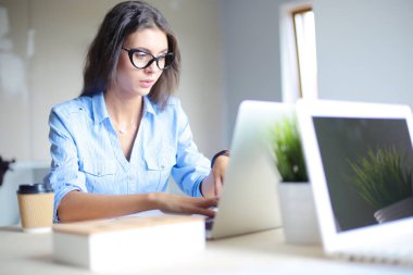 Ofis masasında oturan genç bir kadın dizüstü bilgisayar ekranına bakıyor. Genç kadın.