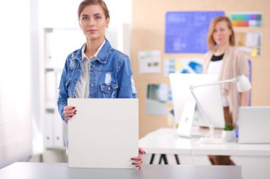 Masanın yanında duran iki genç kadın enstrüman, plan ve dizüstü bilgisayarla.