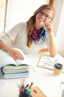 Kitapların arasında bir masada oturan genç bir kadın. Öğrenci