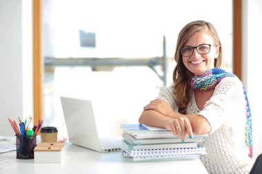 Kitapların arasında bir masada oturan genç bir kadın. Öğrenci
