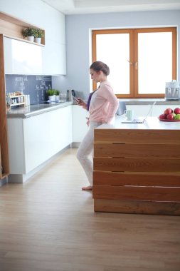 Cep telefonu ayakta modern mutfak kullanan kadın.