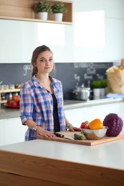 Masanın yanındaki mutfakta sebze doğrayan genç bir kadın..