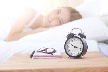 Genç kadın ve çalar saat evde yatak odasında uyuyor. Genç uyuyan kadın.