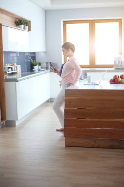 Cep telefonu ayakta modern mutfak kullanan kadın.