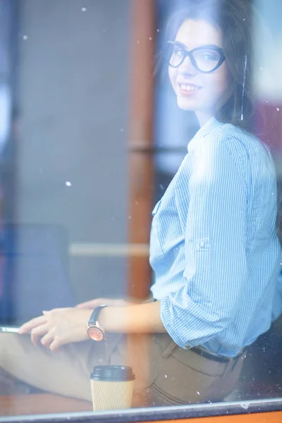 Młoda kobieta siedząca przy stole biurowym z laptopem, z widokiem przez okno. Młoda kobieta — Zdjęcie stockowe