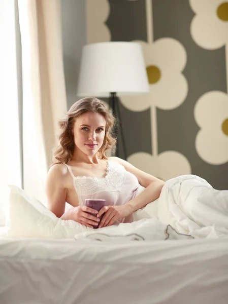 Junge Frau trinkt Kaffee oder Tee im Bett. — Stockfoto