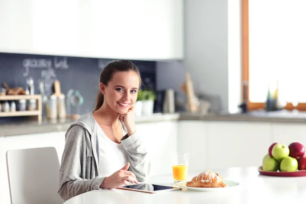 Ung kvinna med apelsinjuice och tablett i köket. — Stockfoto