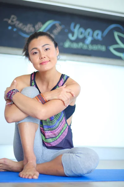 Portræt af den smilende yogakvinde, der sidder på yogamåtten efter træning i yoga studiet. Yoga. Kvinde . - Stock-foto