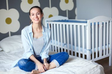 Yatakta çocuk karyolası yakın oturan bir genç bayan. Genç anne