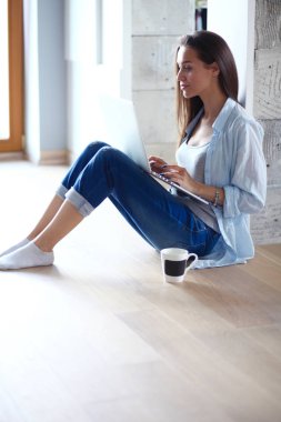 Dizüstü bilgisayar ile yerdeki genç güzel kadın evde oturuyor. Genç güzel kadın.