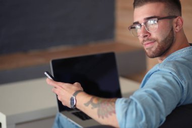 Genç bir telefonu kullanarak ve bir dizüstü bilgisayarda çalışan adam. Öğrenci manifatura telefon.