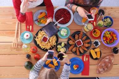 Ahşap masada otururken birlikte yemek yiyen bir grup insanın üst düzey görüntüsü. Masada yemek var. İnsanlar fast food yiyor..