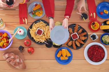 Ahşap masada otururken birlikte yemek yiyen bir grup insanın üst düzey görüntüsü. Masada yemek var. İnsanlar fast food yiyor..