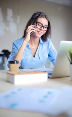 Ofis masasında oturan ve cep telefonuyla konuşan genç ve güzel bir iş kadını. İş kadını