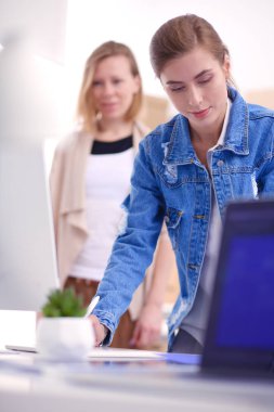 Masanın yanında duran iki genç kadın enstrüman, plan ve dizüstü bilgisayarla.