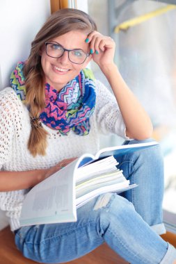 Kitapların arasında bir masada oturan genç bir kadın. Öğrenci