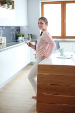 Cep telefonu ayakta modern mutfak kullanan kadın.