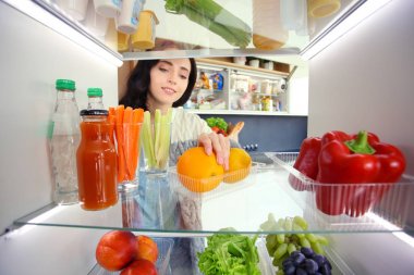 Sağlıklı yiyecek, sebze ve meyvelerle dolu açık buzdolabının yanında duran kadın portresi. Kadın portresi