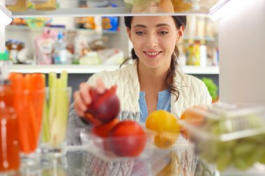Sağlıklı yiyecek, sebze ve meyvelerle dolu açık buzdolabının yanında duran kadın portresi. Kadın portresi
