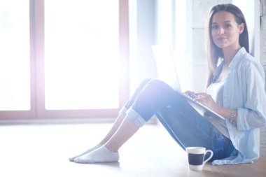 Dizüstü bilgisayar ile yerdeki genç güzel kadın evde oturuyor. Genç güzel kadın.