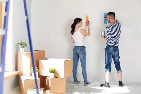 Portret van een vrolijk glimlachend jong stel dat de binnenmuur van een nieuw huis schildert. jong stel — Stockfoto