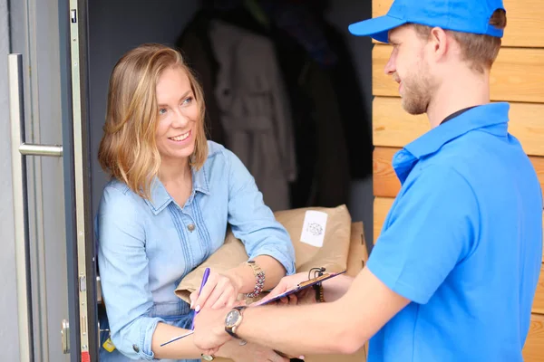 Repartidor sonriente con uniforme azul que entrega la caja de paquetes al destinatario: concepto de servicio de mensajería. Repartidor sonriente en uniforme azul — Foto de Stock