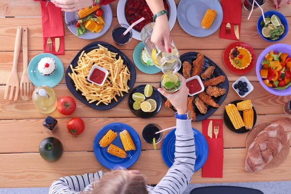 Ahşap masada otururken birlikte yemek yiyen bir grup insanın üst düzey görüntüsü. Masada yemek var. İnsanlar fast food yiyor..