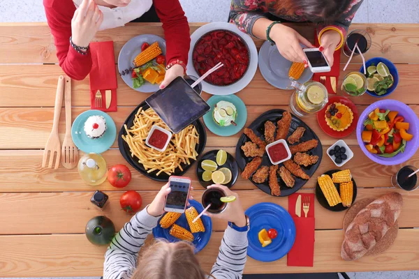 Ahşap masada otururken birlikte yemek yiyen bir grup insanın üst düzey görüntüsü. Masada yemek var. İnsanlar fast food yiyor..