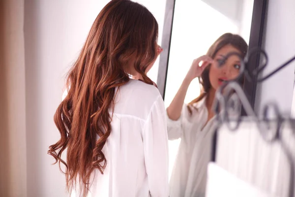 Молода жінка дивиться на себе в дзеркало вдома. Молода жінка . — стокове фото